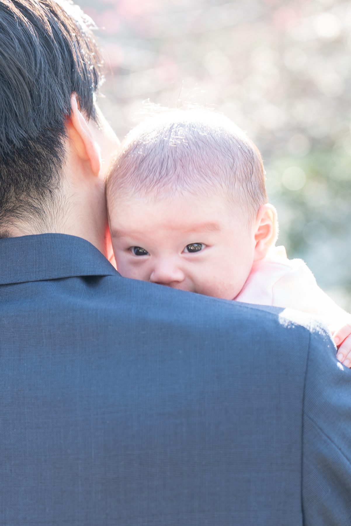 父親の肩越しにこちらを見る赤ちゃん